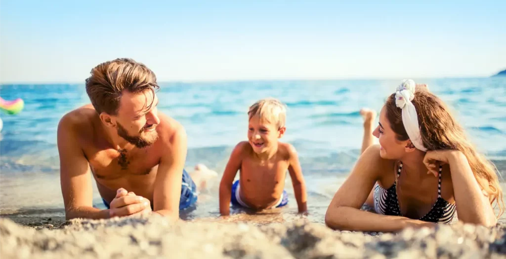 Familie entspannt lachend am sonnigen Strand in Montenegro, mit kristallklarem Meer im Hintergrund
