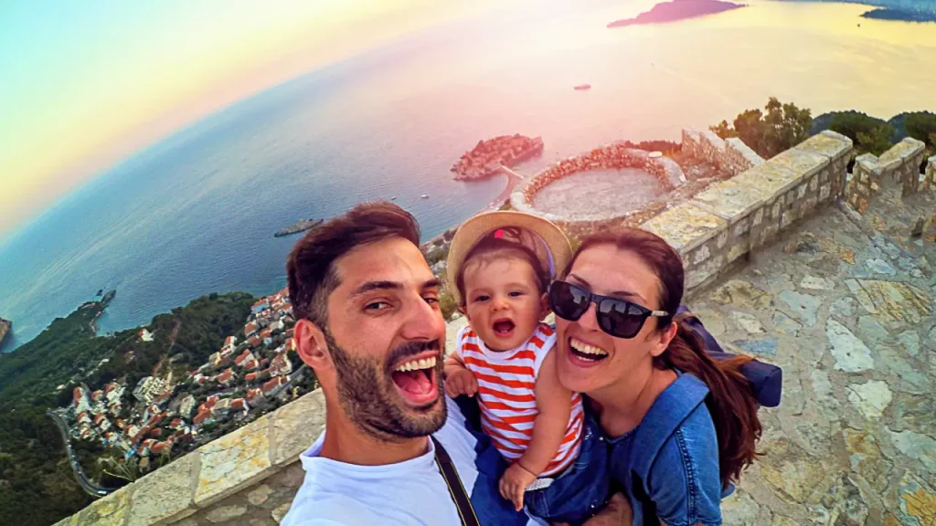 Glückliche Familie macht ein Selfie auf einer alten Festung mit Blick auf Sveti Stefan in Montenegro bei Sonnenuntergang