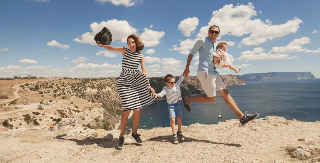 Ausgelassene Familie springt vor freudiger Meereskulisse auf Berggipfel
