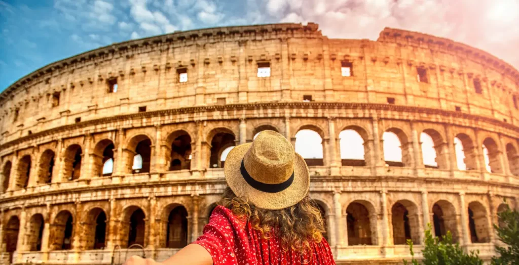 Frau in rotem Kleid mit Strohhut fotografiert sich selbst vor dem Colosseum in Rom, Italien