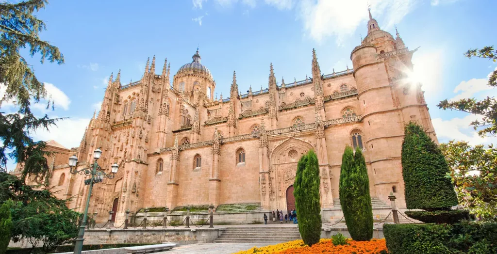 Die Kathedrale namens Catedral Vieja von Salamanca in Spanien, umgeben von gepflegten Gärten und beleuchtet durch die Sonne, die hinter dem Gebäude hervorblitzt