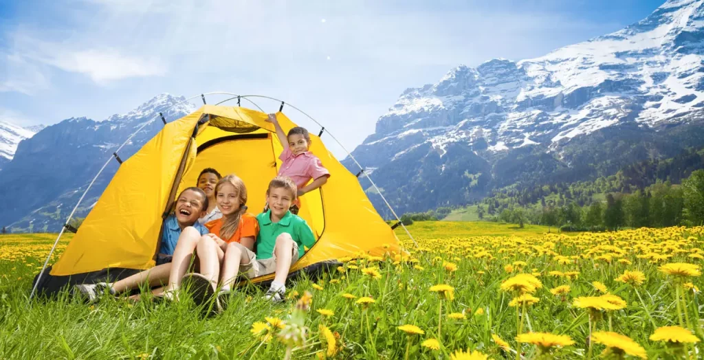Kinder lachen und spielen in einem Zelt auf einer Wiese mit Blick auf die Schweizer Alpen