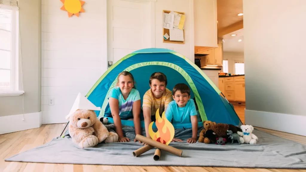 Kinder lächeln im Spielzelt mit Plüschtieren im Wohnzimmer