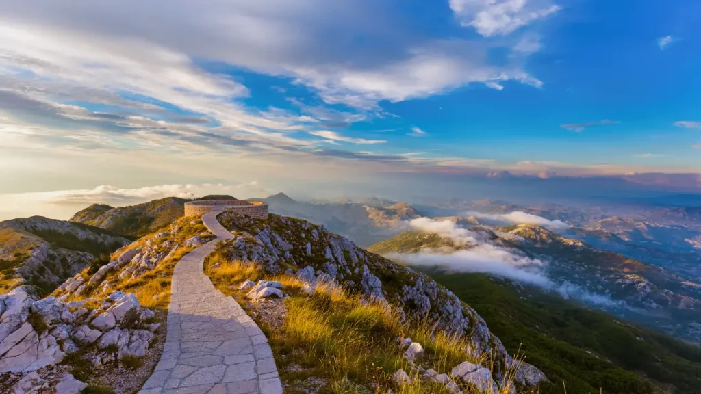 Geschwungener Weg auf den Lovcen Bergen im Nationalpark Montenegro, umgeben von üppigen Graslandschaften und mystischen Wolken