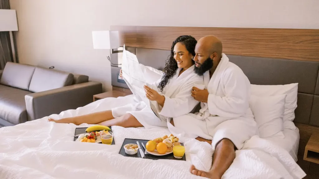 Paar genießt ein Frühstück im Bett in einem gemütlichen Hotelzimmer 
[Bildquelle: © Susannah Townsend | Canva]