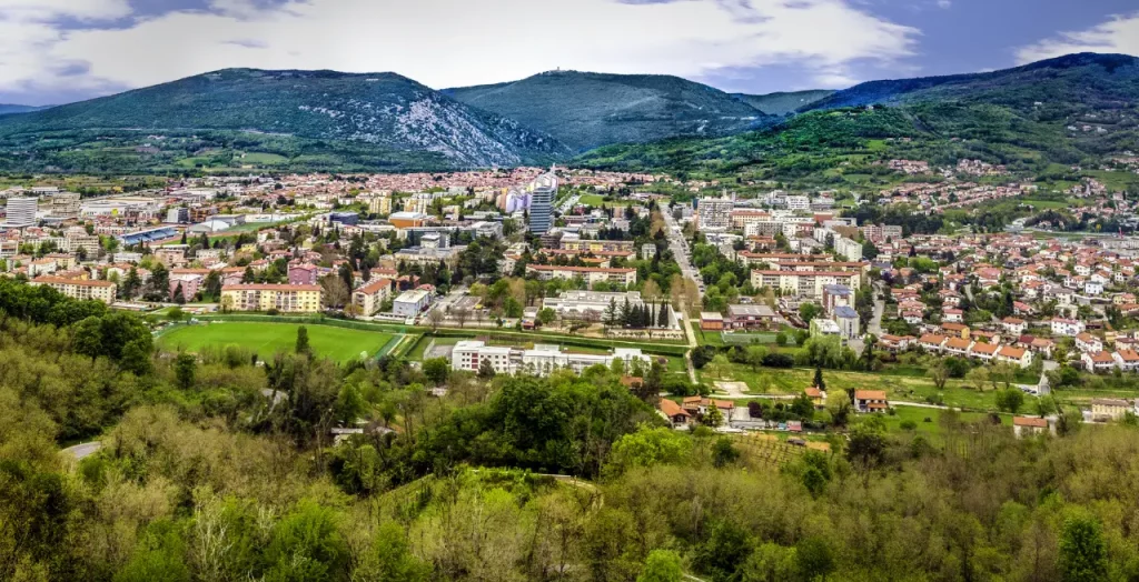 Panoramaaufnahme von Nova Gorica, Slowenien, mit üppigen grünen Hügeln im Hintergrund und städtischer Architektur im Vordergrund [Bildquelle: © premat | Canva]