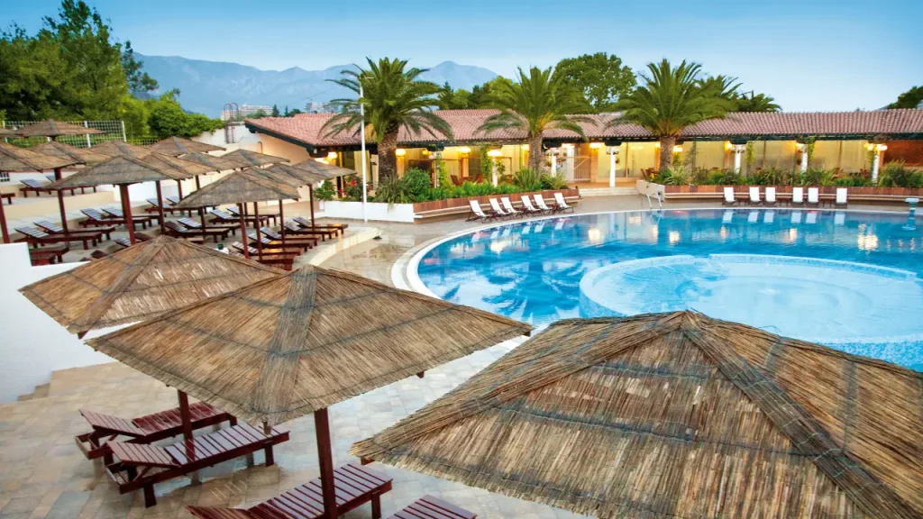Poolbereich der Ferienanlage Slovenska Plaza in Montenegro, umgeben von Strohschirmen und Liegestühlen mit Bergblick [Bildquelle: © Hotel Slovenska Plaza]
