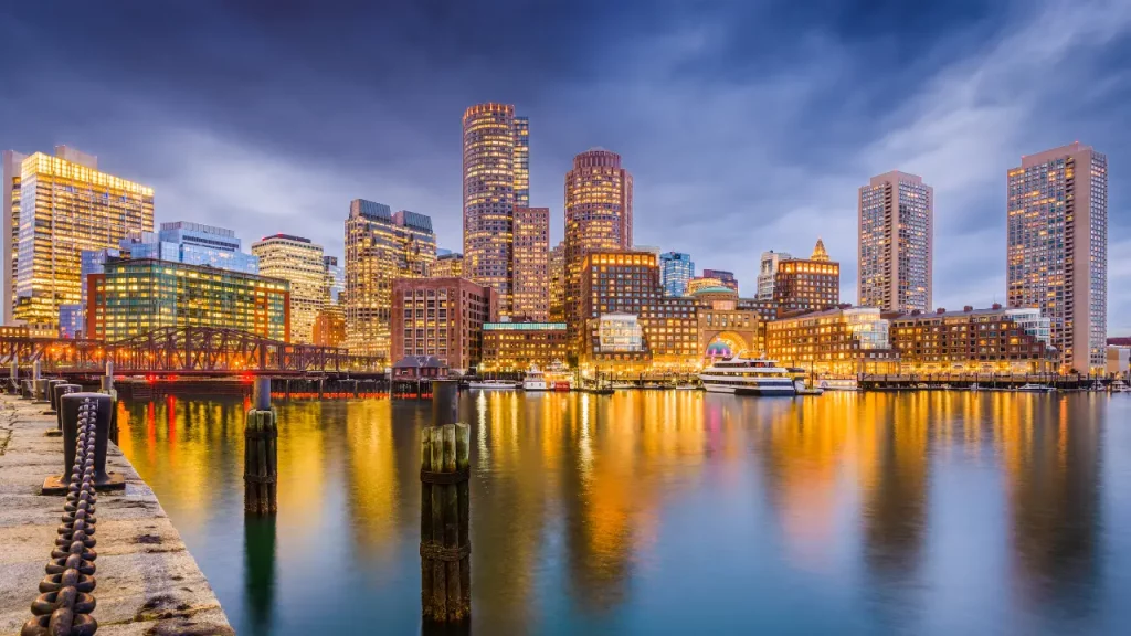 Skyline und Hafen von Boston, Massachusetts bei Dämmerung mit Spiegelungen im Wasser [Bildquelle: © Sean Pavone | Canva]