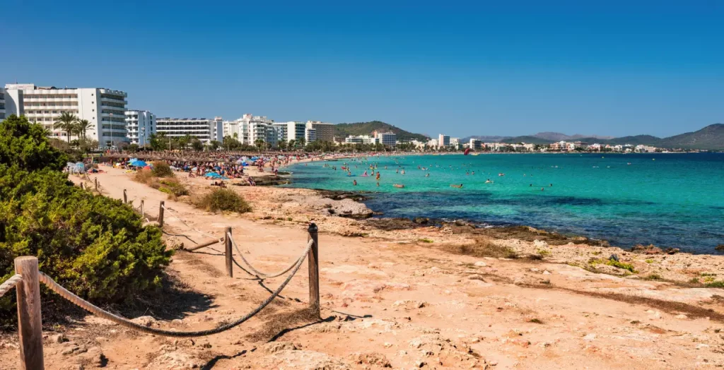 Trockene Küstenlandschaft und türkisfarbenes Wasser vor der Hotelkulisse von Cala Millor, Mallorca