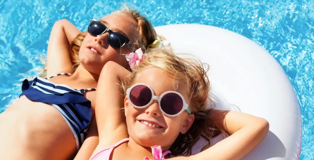 Zwei Kinder entspannen lächelnd auf einem Schwimmreifen im Pool, mit klarem blauem Wasser