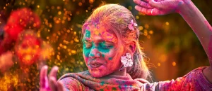 Frau beim Holi Festival in Indien, die mit buntem Pulver bedeckt ist und freudig tanzt.